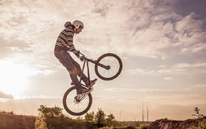 Ein Freeride-Fahrer in der Mitte eines hohen Sprungs, das Fahrrad unter ihm schräg zum Himmel ragend, während das warme Licht der untergehenden Sonne die Szene umrahmt.